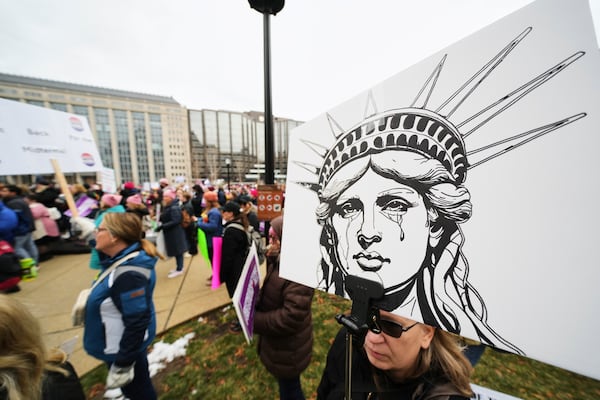 A person holds a sign of a crying Statue of Liberty as a group gathers at Franklin Park before the People's March, Saturday, Jan. 18, 2025, in Washington. (AP Photo/Julio Cortez)