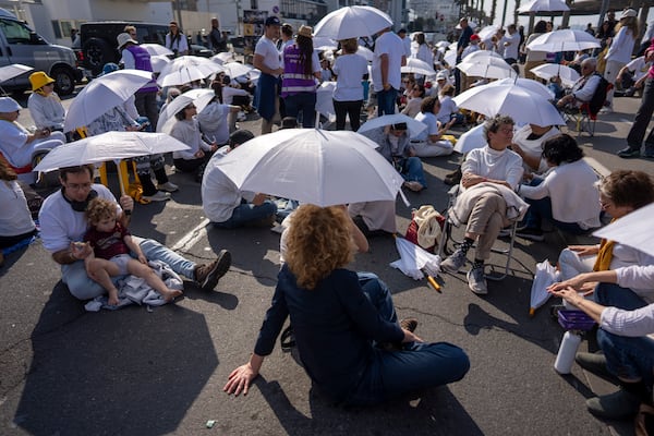 Activists sit on a road with white umbrellas during a protest calling for the release of hostages held in the Gaza Strip, in front of the U.S. Embassy branch office in Tel Aviv, Israel, Friday, Jan. 31, 2025. (AP Photo/Oded Balilty)