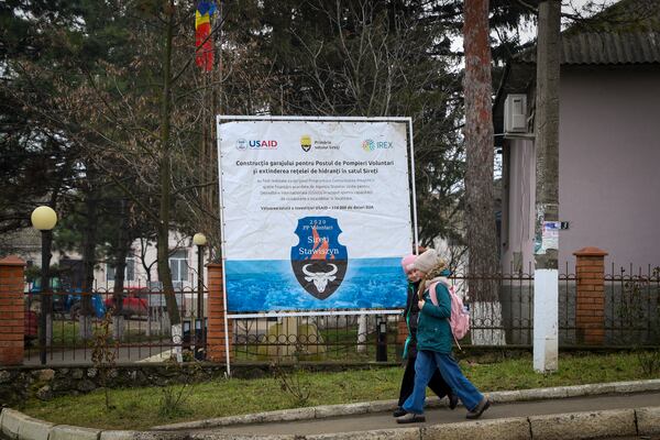 Children walk by a banner presenting a USAID supported project for the extension of the fire hidrants network in the village of Sireti, Moldova, Thursday, Jan. 30, 2025. (AP Photo/Aurel Obreja)