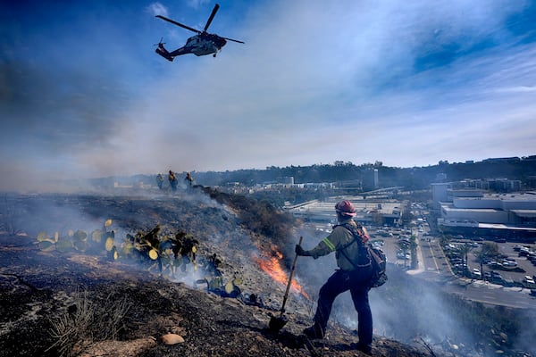 San Diego firefighters knock down a small brush along a hillside over the Mission Valley Shopping Mall in San Diego on Tuesday, Jan. 21, 2025. (AP Photo/Gregory Bull)