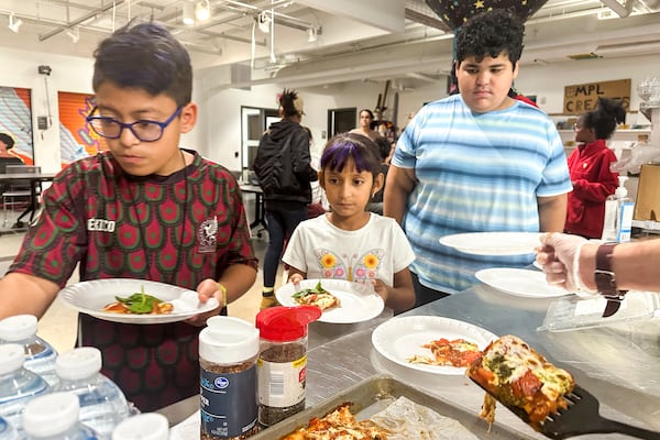 Attendees of the after school nutrition program, Milwaukee Public Library Snack Hack, line up to get a slice of pizza made from scratch, Nov. 19, 2024, in Milwaukee. (AP Photo/Devi Shastri)