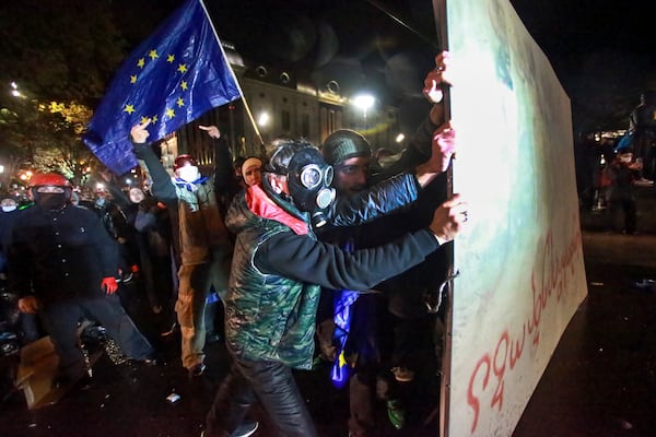 People with an EU flag hold a part of a fence as police use a water cannon to prevent protesters pouring into the streets following Georgian Prime Minister Irakli Kobakhidze's announcement, rallying outside the parliament building in Tbilisi, Georgi, on Friday, Nov. 29, 2024. (AP Photo/Zurab Tsertsvadze)