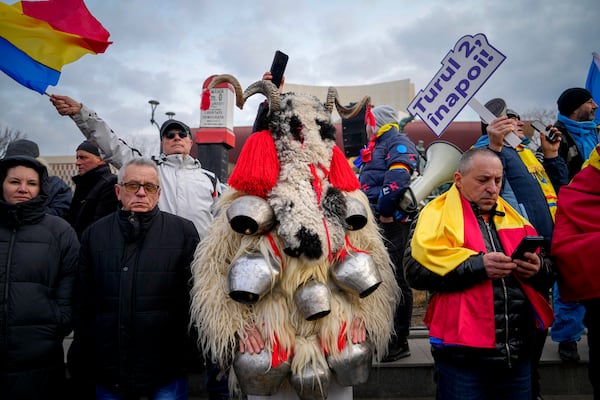 A person dressed in a costume made out of fur stands next to people waving flags and holding a banner that reads "Give us back the second round!" during a rally organized by the right wing Alliance for the Unity of Romanians (AUR), calling for free elections after Romania' s Constitutional Court annulled the first round of presidential elections last December, in Bucharest, Romania, Sunday, Jan. 12, 2025. (AP Photo/Vadim Ghirda)