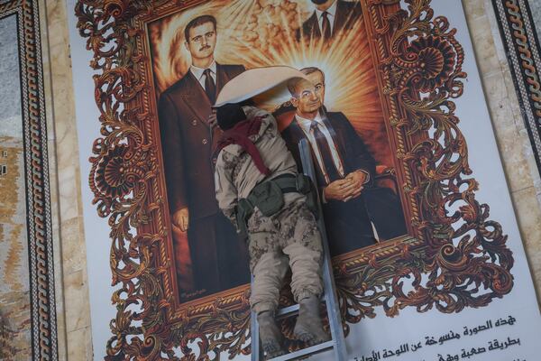 A Syrian opposition fighter tears up a painting depicting Syrian President Bashar Assad and his late father Hazef Assad at the Aleppo international airpot in Aleppo, Syria, Monday, Dec. 2, 2024. .(AP Photo/Omar Albam)