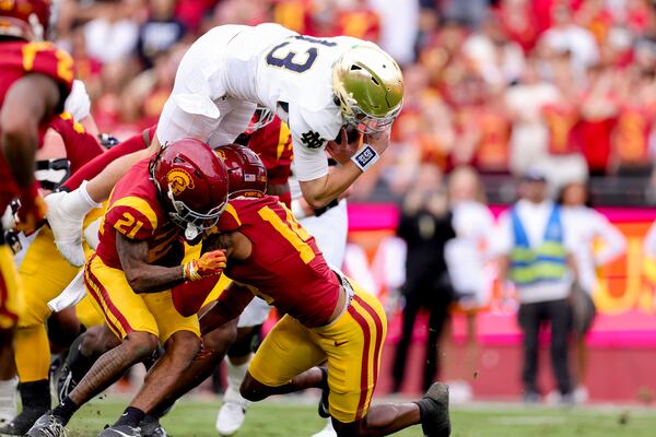 Notre Dame quarterback Riley Leonard, top, dives over Southern California cornerback Greedy Vance Jr., left, and cornerback Jacobe Covington during the first half of an NCAA football game, Saturday, Nov. 30, 2024, in Los Angeles. (AP Photo/Ryan Sun)