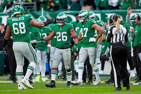 Philadelphia Eagles running back Saquon Barkley (26) is congratulated by offensive tackle Jordan Mailata and teammates after running for a long gain to put him at over 2,000 yards for the season during the second half of an NFL football game against the Dallas Cowboys, Sunday, Dec. 29, 2024, in Philadelphia. (AP Photo/Chris Szagola)