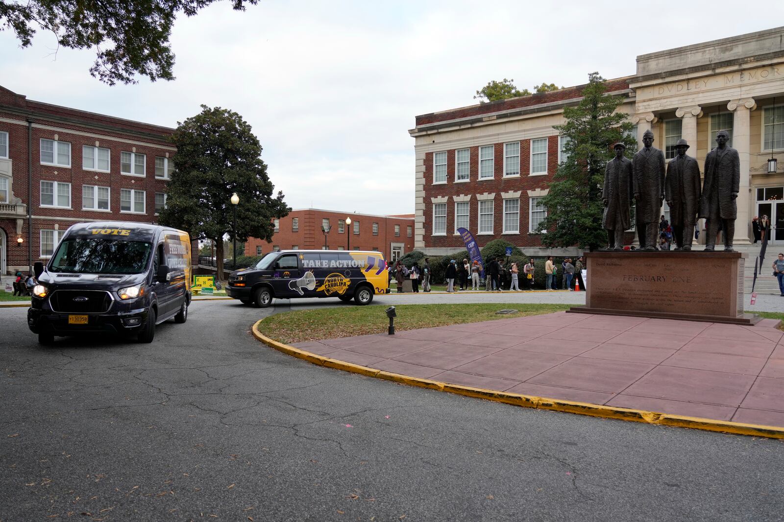 Vans drive around a circle to encourage students to vote in the shadow of a monument of the Greensboro Four protesters at the Dudley Building during a get out the vote rally at North Carolina A&T in Greensboro, N.C., Monday, Oct. 28, 2024. (AP Photo/Chuck Burton)