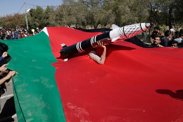 A Houthi supporter carries a mock rocket as he peers from a Palestinian flag during a protest in Sanaa, Yemen, Wednesday, Jan. 22, 2025. (AP Photo/Osamah Abdulrahman)