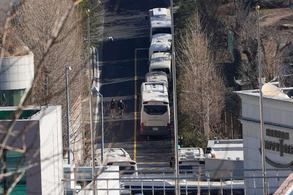 Security personnel walk on a road lined up with buses blocking the entrance gate of impeached South Korean President Yoon Suk Yeol's residence in Seoul, South Korea, Friday, Jan. 10, 2025. (AP Photo/Ahn Young-joon)