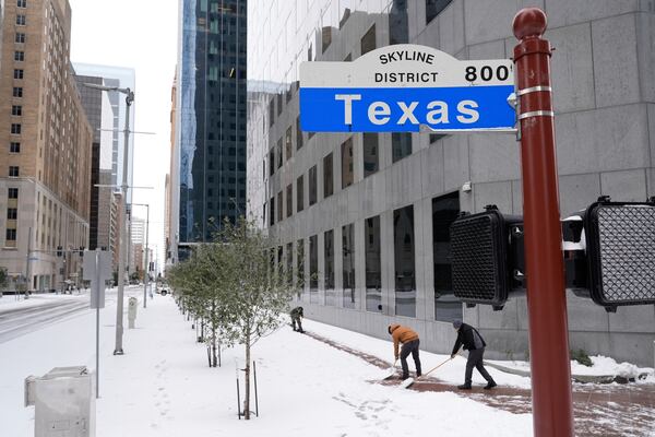 People shovel snow off the sidewalk Tuesday, Jan. 21, 2025, in downtown Houston. (AP Photo/Ashley Landis)