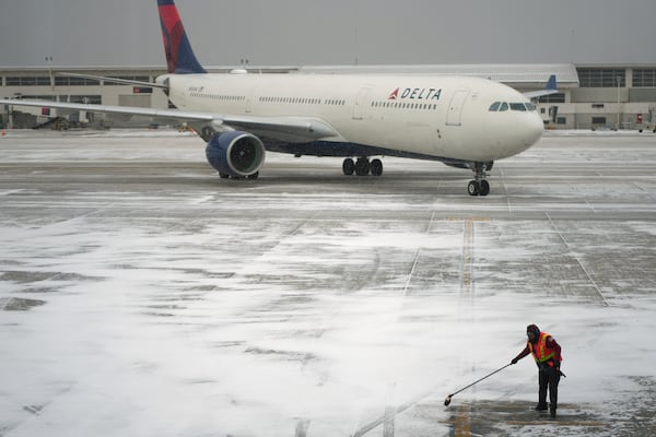 A worker clears snow from an apron before guiding a Delta Air Lines jet at the Detroit Metropolitan Wayne County Airport in Romulus, Mich., Monday, Jan. 6, 2025. (AP Photo/Charlie Riedel)