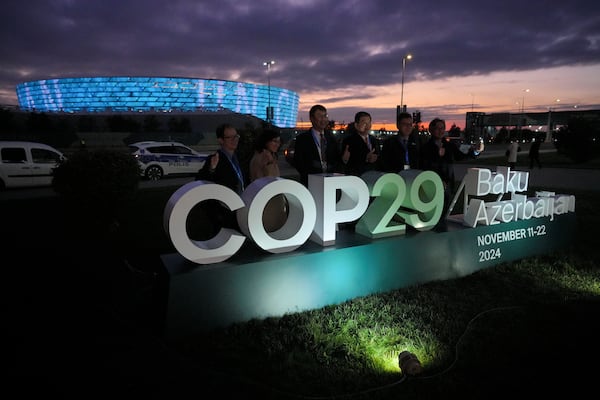 People pose for a photo with the Baku Olympic Stadium in the background at the COP29 U.N. Climate Summit, Thursday, Nov. 14, 2024, in Baku, Azerbaijan. (AP Photo/Peter Dejong)