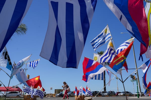 Pedestrians pass by Uruguay's national flag and political party banners for sale on the day of the presidential run-off election in Montevideo, Uruguay, Sunday, Nov. 24, 2024. (AP Photo/Natacha Pisarenko)