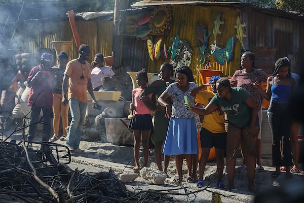 A woman films a scene where the bodies of suspected gang members who were set on fire by residents sit in a heap in the middle of a road, in the Pétion-Ville neighborhood of Port-au-Prince, Haiti, Tuesday, Nov. 19, 2024. (AP Photo/Odelyn Joseph)