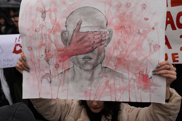 A student holds a banner and stands in silence during ongoing protests that erupted after a concrete canopy fell last month and killed 15 people, in Belgrade, Serbia, Friday, Dec. 20, 2024. (AP Photo/Darko Vojinovic)