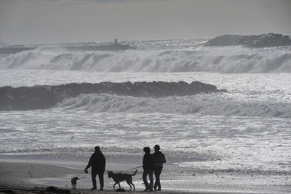 Visitors walk along the beach as high surf comes in Ventura, Calif., Tuesday, Dec. 24, 2024. (AP Photo/Damian Dovarganes)