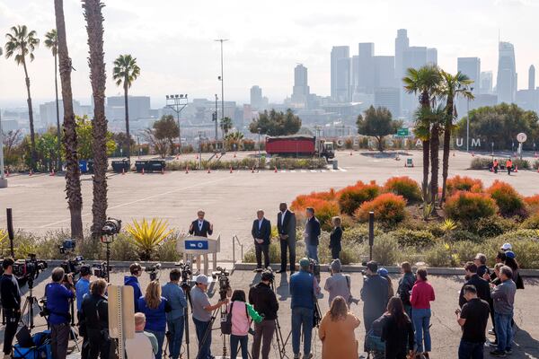 2028 Olympics organizer Casey Wasserman, at podium, introduces Dodgers President and CEO Stan Kasten, from fourth right back, Magic Johnson, and California Gov. Gavin Newsom outside Dodger Stadium overlooking downtown Los Angeles, to announce a new private sector initiative called LA Rises to support rebuilding efforts after the devastating wildfires, Tuesday, Jan. 28, 2025. (AP Photo/Damian Dovarganes)