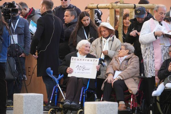 A woman holds a placard reading: "Welcome, 108 year's old the eldest of Ajaccio" as she waits for the arrival of Pope Francis at the Baptistery of St. Jean in Ajaccio during the Pontiff one-day visit in the French island of Corsica, Sunday, Dec. 15, 2024. (AP Photo/Alessandra Tarantino)