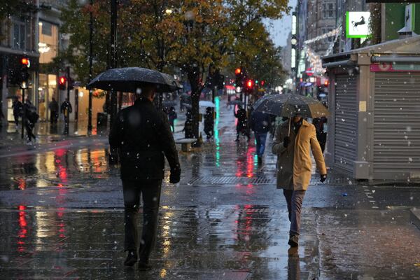 People walk along the Oxford Street as snow falls in London, Tuesday, Nov. 19, 2024. (AP Photo/Kin Cheung)