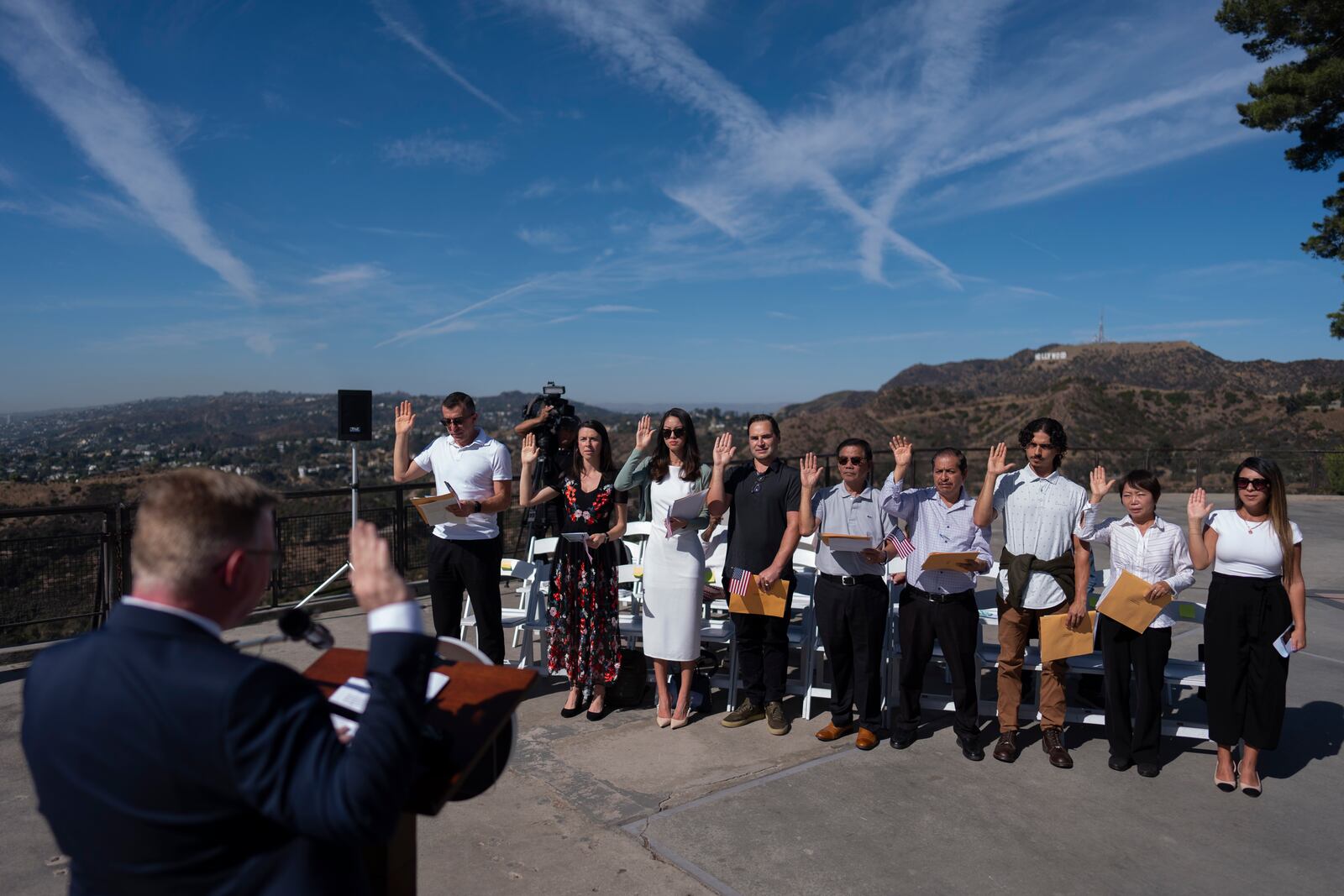 With the Hollywood sign in the background, people raise their hands as they take the Oath of Allegiance to the United States during a naturalization ceremony at Griffith Observatory in Los Angeles, Monday, Oct. 21, 2024. (AP Photo/Jae C. Hong)