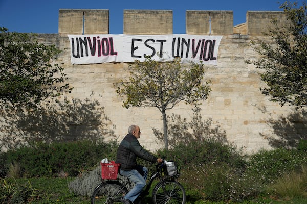 FILE - A man rides a bicycle in front of a banner that reads, "A rape is a rape," in Avignon, southern France, on Oct. 16, 2024. (AP Photo/Lewis Joly, File)