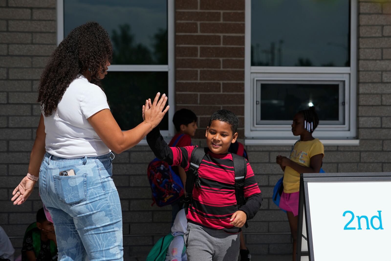 Dylan Martínez-Ramírez, center, high-fives his teacher Aliah James, left, after school Thursday, Aug. 29, 2024, in Aurora, Colo. (AP Photo/Godofredo A. Vásquez)