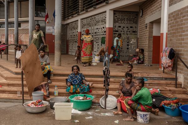 Women wash clothes after a short rain filled their pots with water, at the Lycée des Lumières where they found shelter after losing their homes, in Mamoudzou, Mayotte, Thursday, Dec. 19, 2024 . (AP Photo/Adrienne Surprenant)