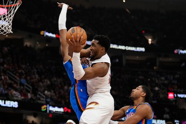 Cleveland Cavaliers guard Donovan Mitchell, center, goes to the basket between Oklahoma City Thunder forward Jalen Williams, left, and guard Aaron Wiggins,in the first half of an NBA basketball game, Wednesday, Jan. 8, 2025, in Cleveland. (AP Photo/Sue Ogrocki)