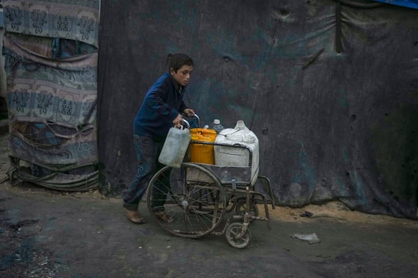 A Palestinian boy pushes a wheelchair carrying jerrycans and plastic bottles with water at a camp for displaced people in Deir al-Balah, Gaza Strip, Thursday, Dec. 12, 2024. (AP Photo/Abdel Kareem Hana)