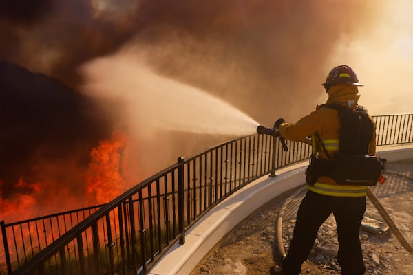 A firefighter makes a stand in front of the advancing Palisades Fire in the Pacific Palisades neighborhood of Los Angeles, Tuesday, Jan. 7, 2025. (AP Photo/Etienne Laurent)