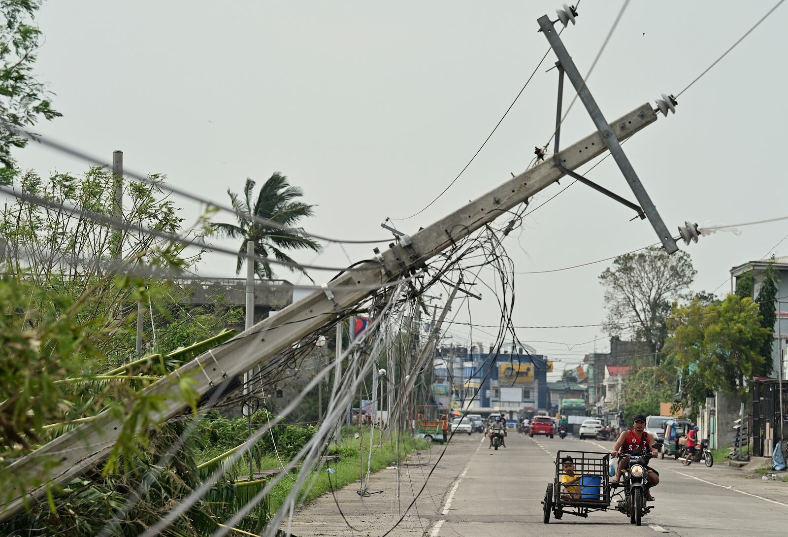 Residents riding a tricycle pass by toppled electrical post caused by Typhoon Yinxing, locally called Marce, in Camalaniugan, Cagayan province, northern Philippines on Friday, Nov. 8, 2024. (AP Photo/Noel Celis)