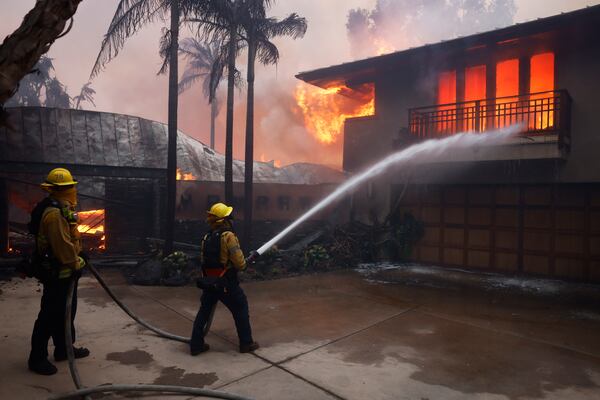 Firefighters hose down flames as the Palisades Fire destroys a residence in the Pacific Palisades neighborhood of Los Angeles, Tuesday, Jan. 7, 2025. (AP Photo/Etienne Laurent)