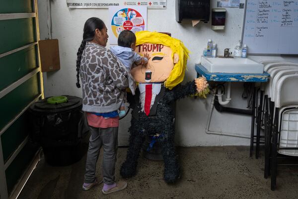 A migrant woman from the Mexican state of Guerrero holds her 1-year-old granddaughter as she hits a piñata of President Donald Trump at a shelter for migrants Wednesday, Jan. 22, 2025, in the border city of Tijuana, Mexico. (AP Photo/Gregory Bull)