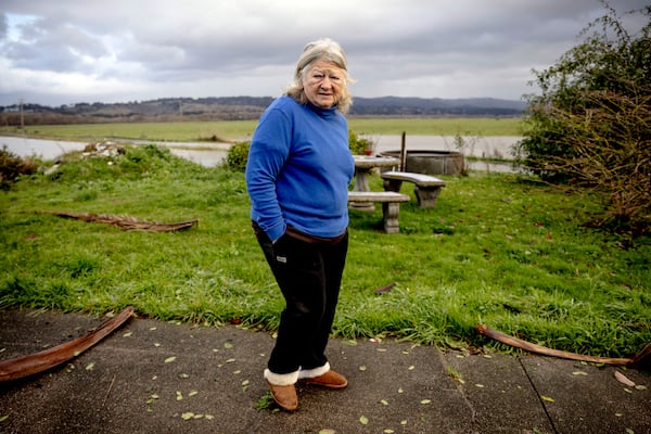 Sharon Scofield, 71, checks the debris in her front yard after winds knocked over many signs and halloween decorations, as flood water from the swollen Eel River is seen in the background in Ferndale, Calif., Friday, Nov. 22, 2024.(Stephen Lam/San Francisco Chronicle via AP)