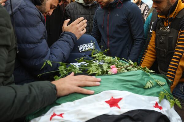 Colleagues and friends mourn over the body, covered with a Syrian opposition flag, of Syrian photographer Anas Alkharboutli, 32, in Idlib, Syria, Wednesday Dec. 4, 2024. Alkharboutli, working for the German news agency DPA was killed in an airstrike near the city of Hama, the agency said Wednesday.(AP Photo/Ghaith Alsayed)