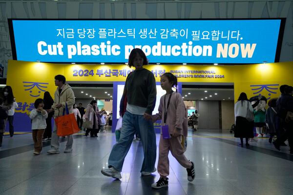 FILE - People pass by a sign calling for a reduction in plastic production near the venue for the fifth session of the Intergovernmental Negotiating Committee on Plastic Pollution in Busan, South Korea, Nov. 30, 2024. (AP Photo/Ahn Young-joon)