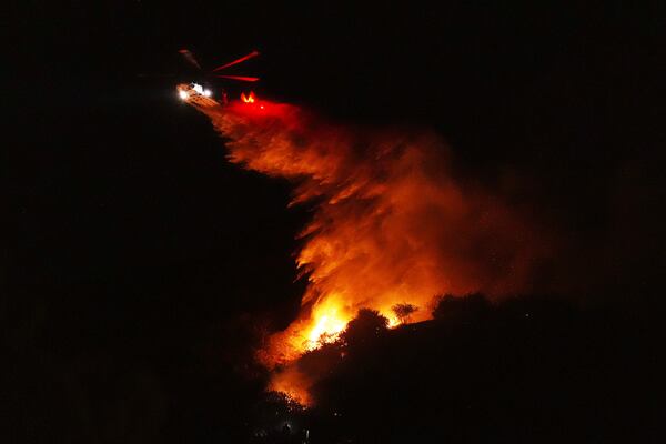 A helicopter drops water on a fire as it burns along Interstate 405, Thursday, Jan. 23, 2025, in Los Angeles. (AP Photo/Mark J. Terrill)