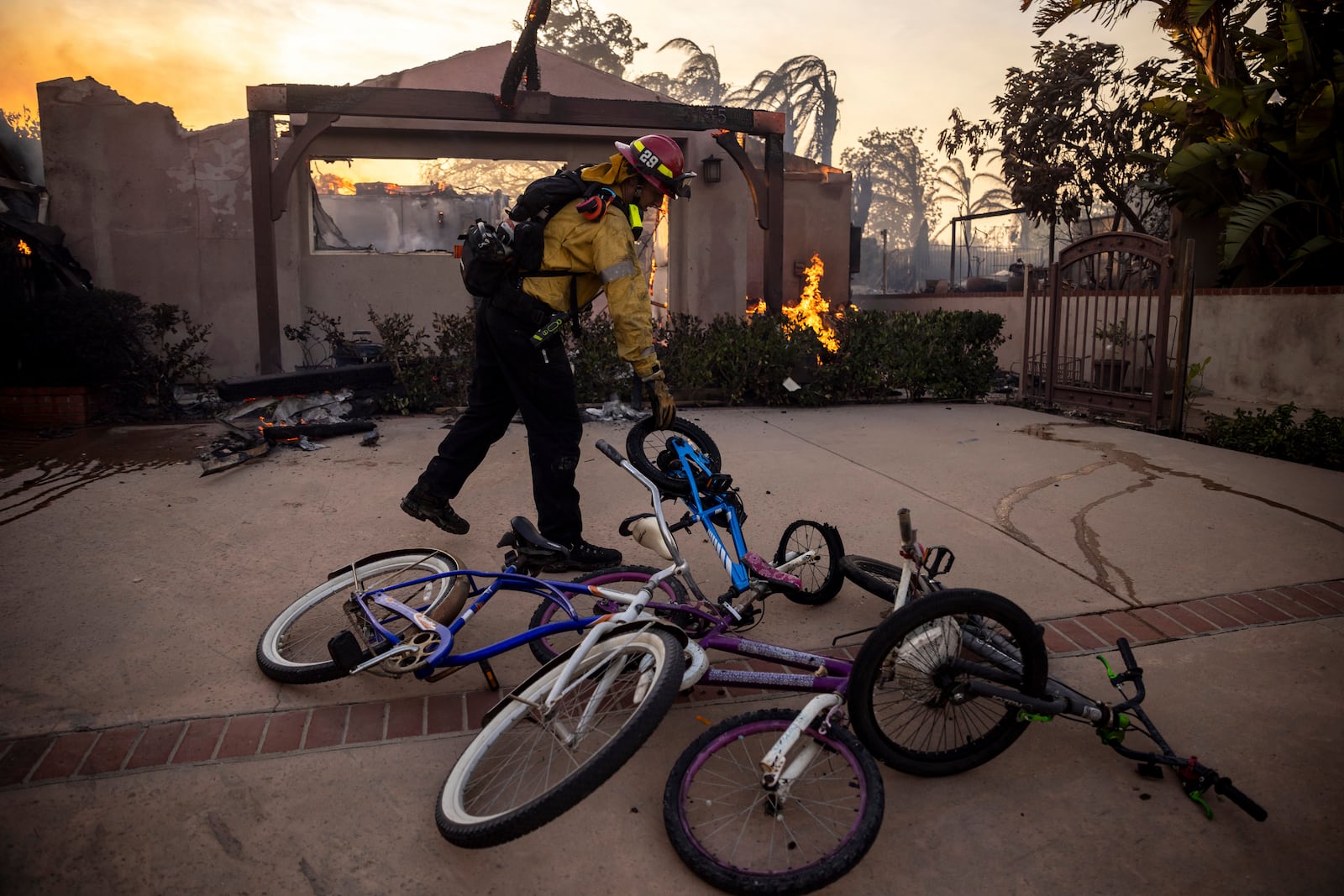 A firefighter, moves bicycles as he works against the Mountain fire, Wednesday, Nov. 6, 2024, near Camarillo, Calif. (AP Photo/Ethan Swope)