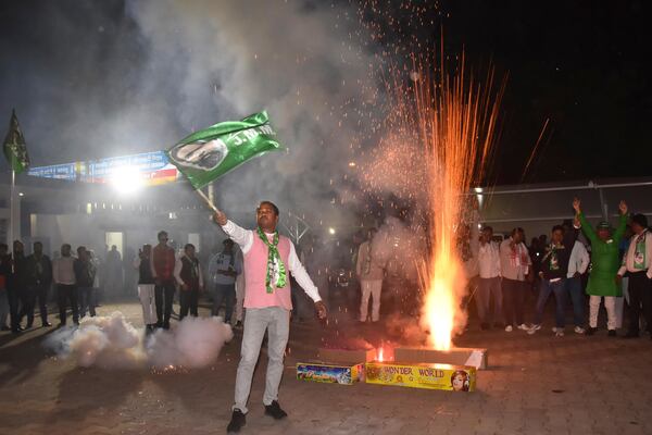 A supporter of Jharkhand Mukti Morcha waves party flag while others burn firecrackers as they celebrate their party's win in state assembly election in Ranchi, in the Indian state of Jharkhand, Saturday, Nov. 23, 2024. (AP Photo/Rajesh Kumar)