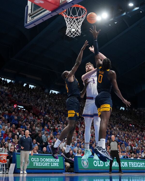 Kansas center Hunter Dickinson (1) shoots between West Virginia guard Toby Okani, left, and center Eduardo Andre (0) during the first half of an NCAA college basketball game, Tuesday, Dec. 31, 2024, in Lawrence, Kan. (AP Photo/Charlie Riedel)