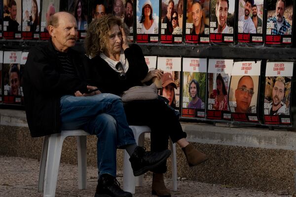 A couple sits beside a display of posters showing hostages held on the Gaza Strip in Tel Aviv, Israel, as Israel's security Cabinet recommended approval of a ceasefire deal after Prime Minister Benjamin Netanyahu confirmed an agreement had been reached that would pause the 15-month war with Hamas in Gaza and release dozens of hostages held by militants there, Friday, Jan. 17, 2025. (AP Photo/Maya Alleruzzo)