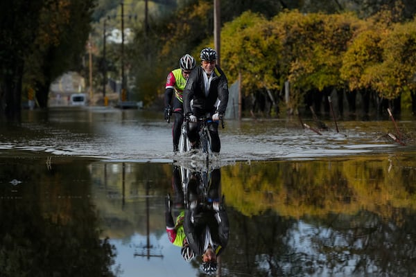 Dave Edmonds, right, and Mike Raasch ride their bicycles on a flooded road Saturday, Nov. 23, 2024, in Windsor, Calif. (AP Photo/Godofredo A. Vásquez)