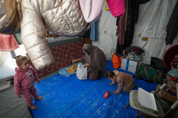 Wafaa Nasrallah places bread on a tray as her 4-year-old son, Ameer, plays nearby and her 2-year-old daughter, Ayloul, stands at their tent in a camp for displaced Palestinians in Deir al-Balah, Gaza Strip, Saturday Dec. 28, 2024. (AP Photo/Abdel Kareem Hana)