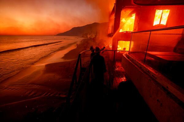 Firefighters work from a deck as the Palisades Fire burns a beachfront property Wednesday, Jan. 8, 2025 in Malibu, Calif. (AP Photo/Etienne Laurent)