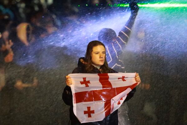 A demonstrator with a Georgian national flag stands under running water from a water cannon rallying outside the parliament's building to continue protests against the government's decision to suspend negotiations on joining the European Union in Tbilisi, Georgia, on Monday, Dec. 2, 2024.(AP Photo/Zurab Tsertsvadze)