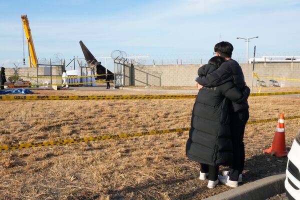 Mourners watch the site of a plane fire from outside of Muan International Airport in Muan, South Korea, Monday, Dec. 30, 2024. (AP Photo/Ahn Young-joon)