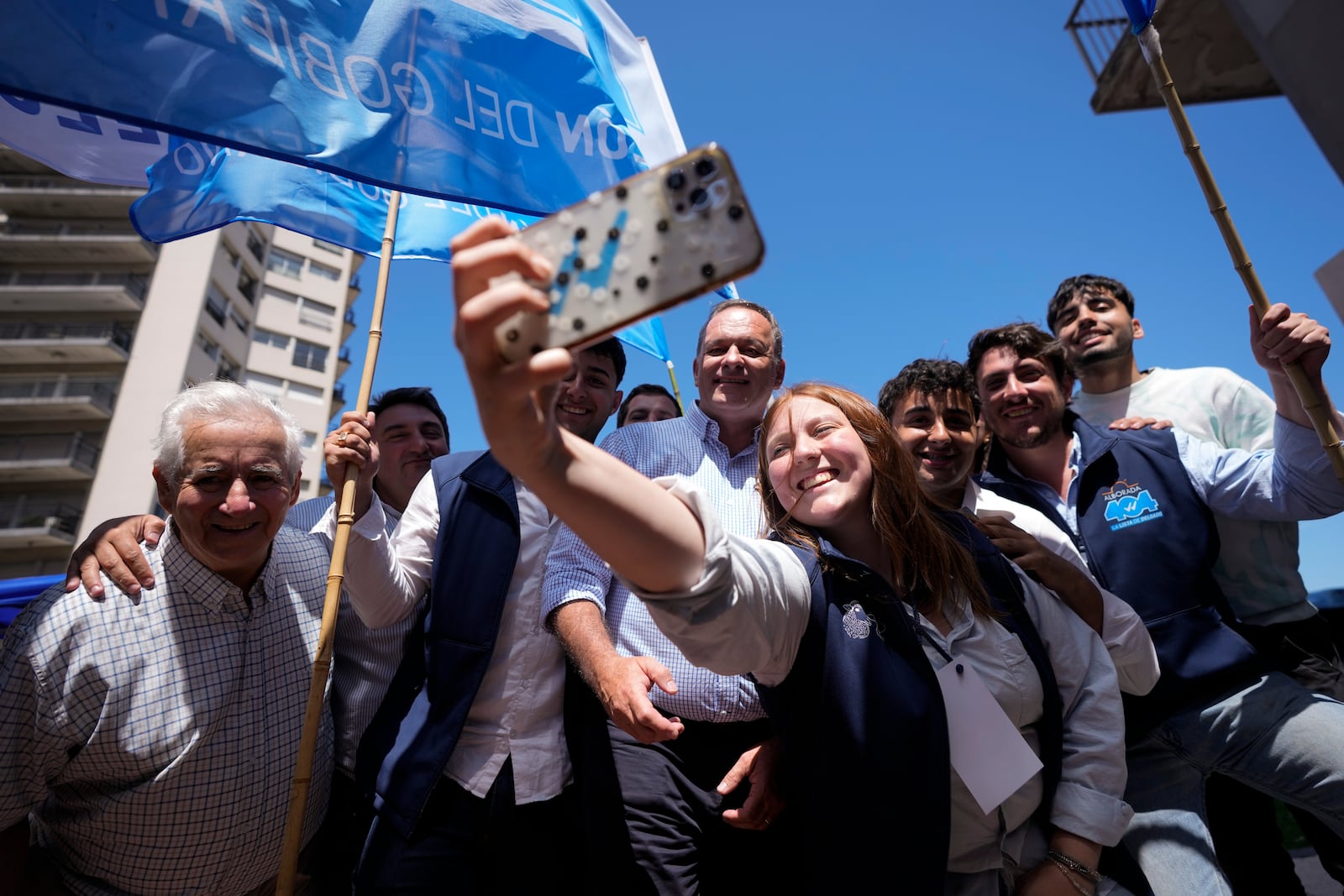 Alvaro Delgado, presidential candidate for the ruling National Party, center, poses for a selfie with supporters outside a polling station during general elections in Montevideo, Uruguay, Sunday, Oct. 27, 2024. (AP Photo/Natacha Pisarenko)