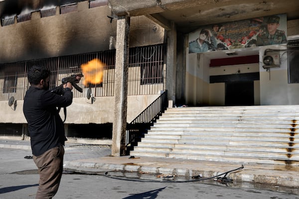 A Syrian fighter from rebel group, fires towards a poster at the entrance of the notorious security detention centre called Palestine Branch, which pictures the late Syrian President Hafez Assad and his son the ouster Syrian president Bashar Assad, in Damascus, Syria, Saturday, Dec. 14, 2024. (AP Photo/Hussein Malla)