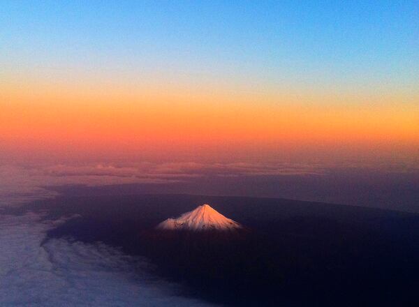 FILE - New Zealand's Mount Taranaki, also known as Mount Egmont, has a warm glow lighting the snow peak, June 12, 2011. (AP Photo/David Frampton, File)