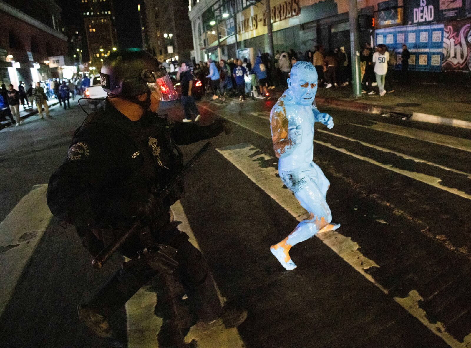 A person covered in blue paint runs from a police officer as fans celebrate on streets after the Los Angeles Dodgers won against the New York Yankees in the baseball World Series Wednesday, Oct. 30, 2024, in Los Angeles. (AP Photo/Ethan Swope)